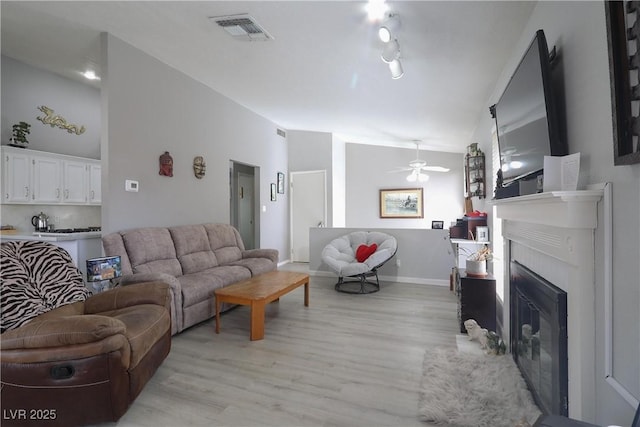 living area featuring visible vents, light wood-style flooring, a glass covered fireplace, baseboards, and ceiling fan