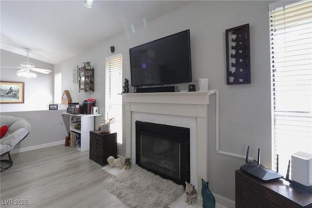 living area with a ceiling fan, a tiled fireplace, wood finished floors, a healthy amount of sunlight, and vaulted ceiling