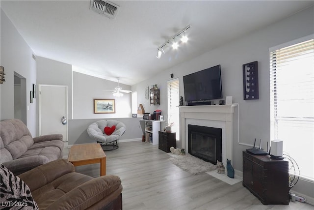 living area with wood finished floors, visible vents, a fireplace with flush hearth, ceiling fan, and vaulted ceiling