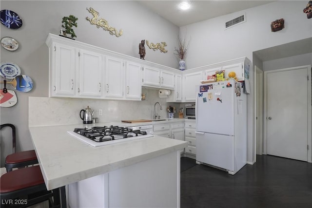 kitchen with visible vents, light countertops, a peninsula, white appliances, and a sink