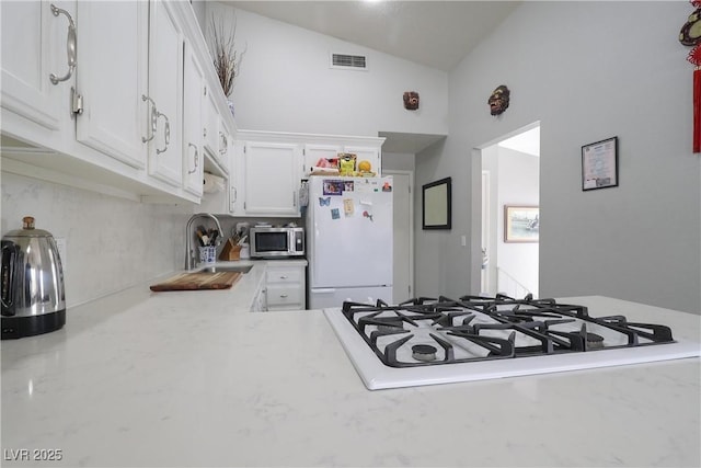 kitchen featuring white appliances, visible vents, lofted ceiling, a sink, and white cabinets