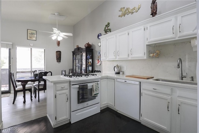 kitchen featuring light countertops, a peninsula, white appliances, white cabinetry, and a sink