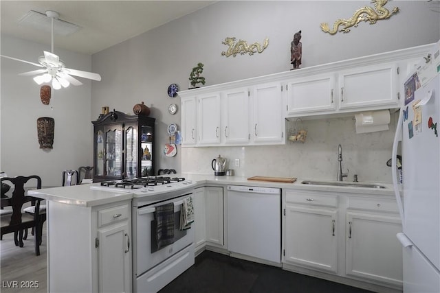 kitchen with light countertops, a peninsula, white cabinets, white appliances, and a sink