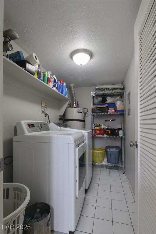 clothes washing area featuring washer and dryer, a textured ceiling, water heater, light tile patterned flooring, and laundry area