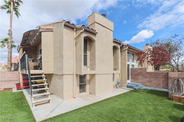 rear view of property with fence, stairs, stucco siding, a lawn, and a chimney