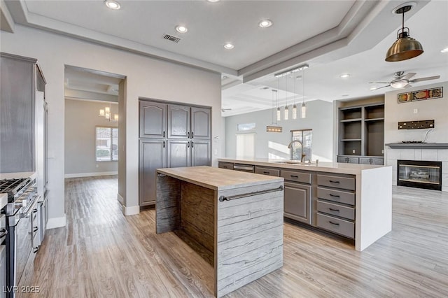 kitchen with visible vents, an island with sink, stainless steel range with gas stovetop, gray cabinetry, and a sink