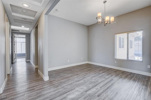 spare room featuring an inviting chandelier, wood finished floors, and baseboards