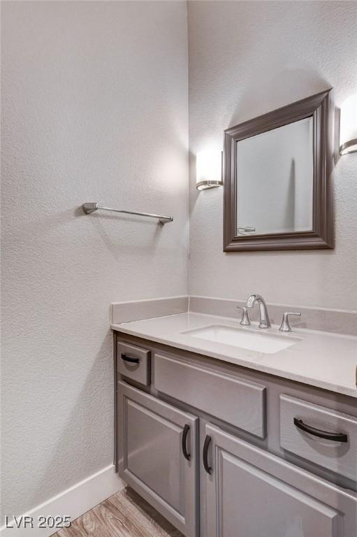 bathroom featuring a textured wall, vanity, baseboards, and wood finished floors