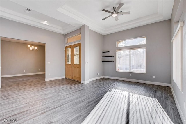 unfurnished living room with wood finished floors, baseboards, visible vents, a tray ceiling, and ceiling fan with notable chandelier