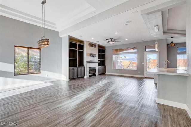 unfurnished living room featuring a glass covered fireplace, a healthy amount of sunlight, a sink, and dark wood-style flooring