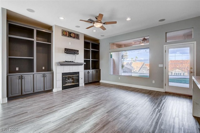 unfurnished living room with wood finished floors, recessed lighting, a fireplace, baseboards, and ceiling fan