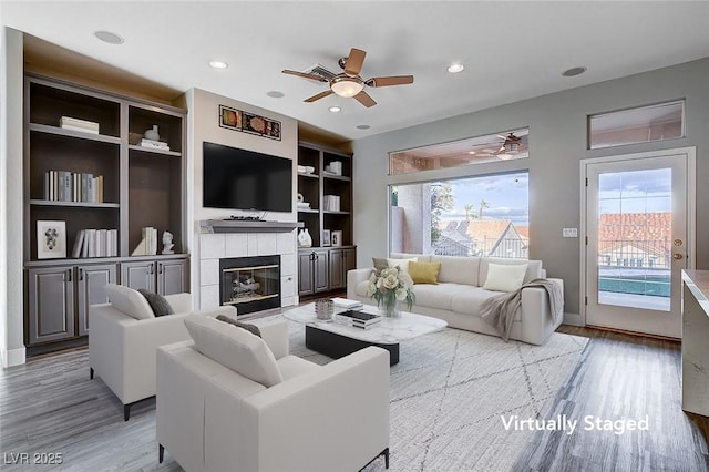 living area featuring a tiled fireplace, recessed lighting, light wood finished floors, and a ceiling fan