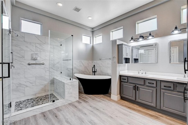 bathroom with visible vents, wood finished floors, a stall shower, a freestanding tub, and a sink