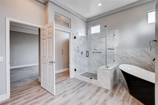 full bathroom with wood finished floors, baseboards, a freestanding tub, a shower stall, and tile walls