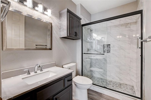 bathroom featuring vanity, wood finished floors, a stall shower, toilet, and a textured wall