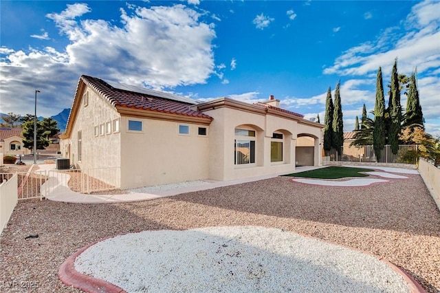 rear view of property featuring a tiled roof, stucco siding, solar panels, and a fenced backyard