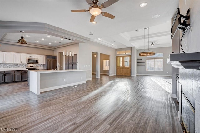 kitchen featuring wood finished floors, decorative backsplash, light countertops, stainless steel microwave, and open floor plan