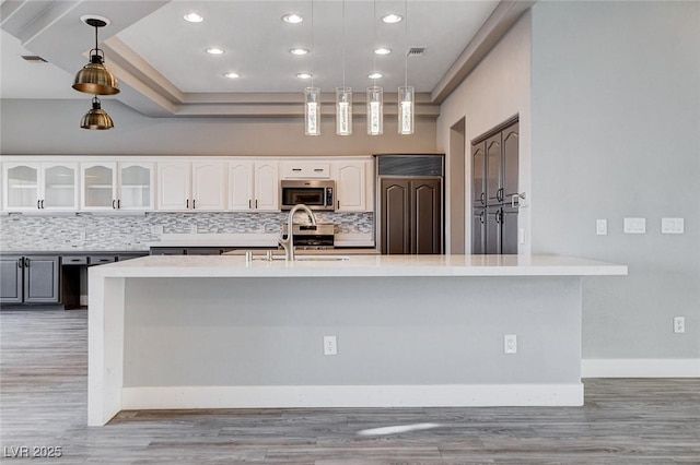 kitchen with decorative backsplash, white cabinetry, stainless steel appliances, light countertops, and glass insert cabinets