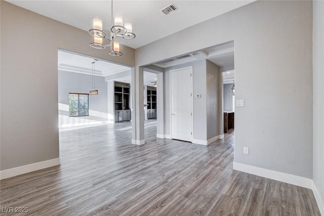 empty room featuring a chandelier, visible vents, baseboards, and wood finished floors