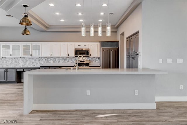 kitchen featuring glass insert cabinets, decorative backsplash, light wood-style flooring, appliances with stainless steel finishes, and white cabinetry