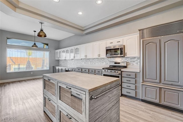 kitchen with light wood-type flooring, backsplash, white cabinetry, appliances with stainless steel finishes, and glass insert cabinets