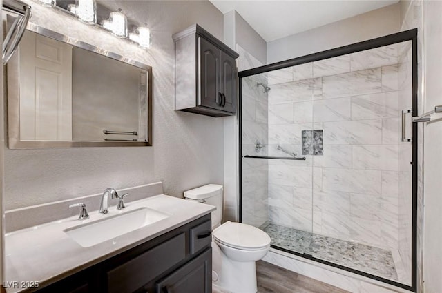 full bathroom with toilet, a stall shower, vanity, and a textured wall