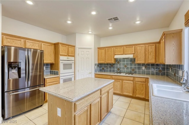 kitchen with visible vents, a sink, tasteful backsplash, a center island, and white appliances