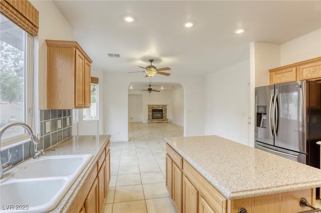 kitchen with visible vents, a kitchen island, ceiling fan, a sink, and stainless steel fridge