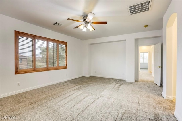carpeted spare room featuring visible vents, baseboards, arched walkways, and ceiling fan