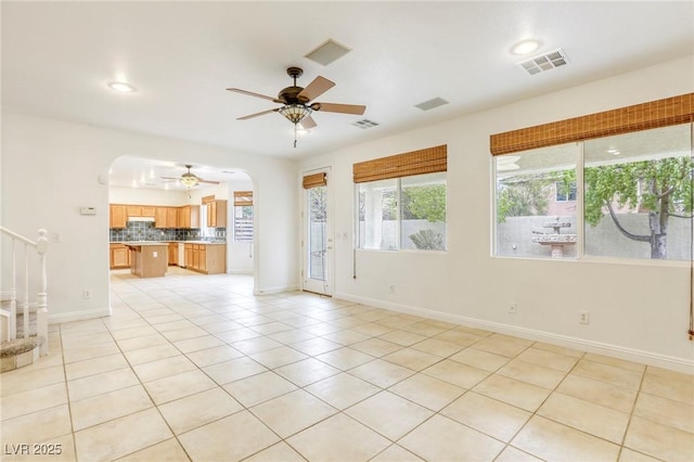 unfurnished living room featuring light tile patterned floors, arched walkways, visible vents, and ceiling fan