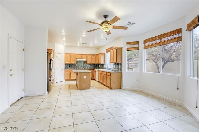 kitchen with tasteful backsplash, visible vents, a kitchen island, light countertops, and stainless steel refrigerator