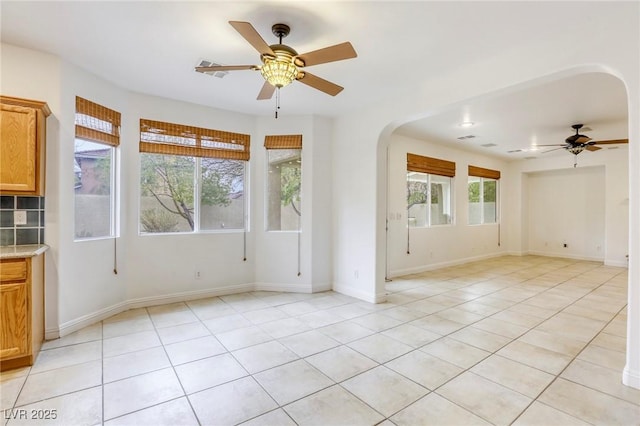 spare room featuring arched walkways, light tile patterned floors, baseboards, and a ceiling fan