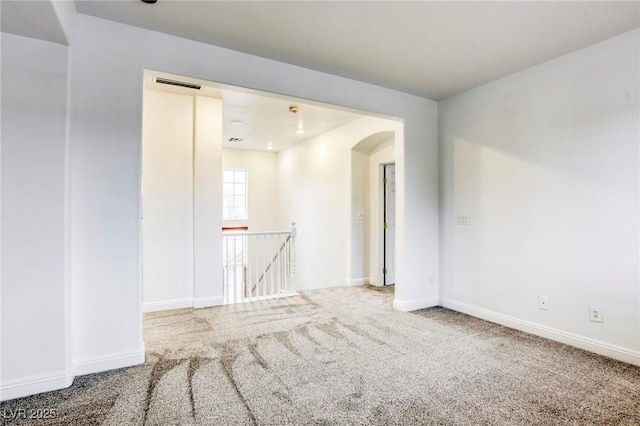 carpeted spare room with visible vents, arched walkways, and baseboards