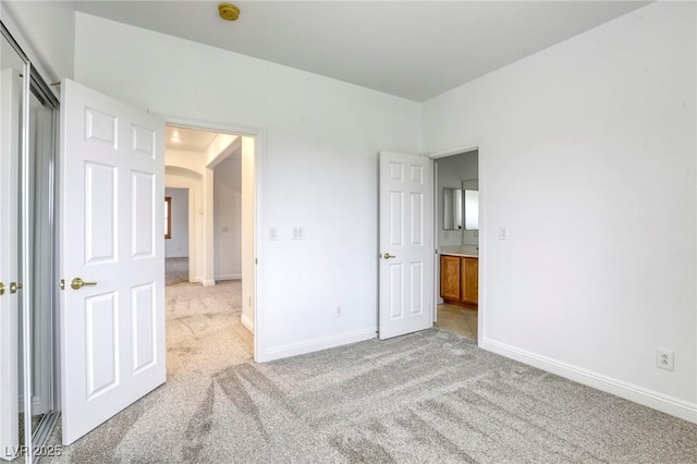unfurnished bedroom with baseboards, arched walkways, and light colored carpet