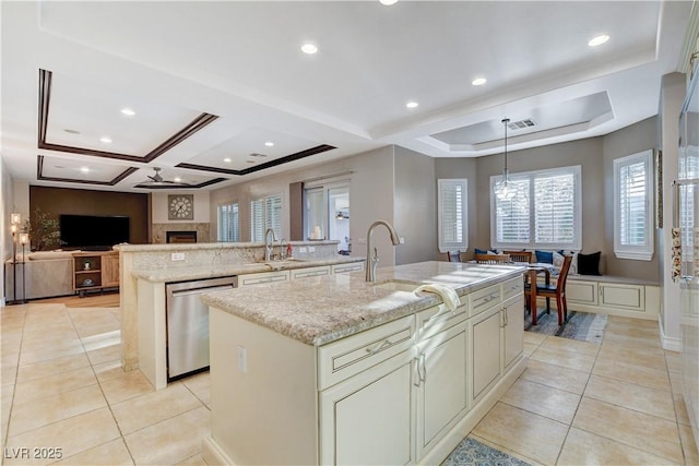 kitchen with light stone counters, stainless steel dishwasher, an island with sink, and light tile patterned flooring