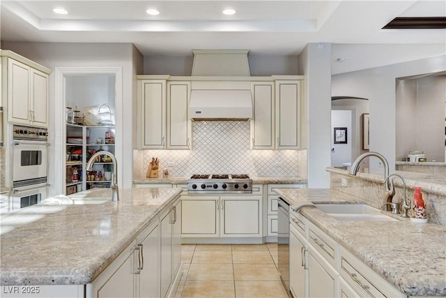 kitchen featuring extractor fan, an island with sink, light tile patterned floors, stainless steel appliances, and a sink