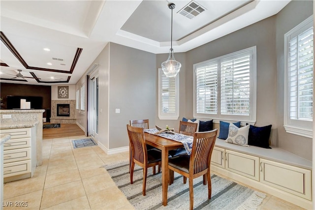 dining room featuring visible vents, a fireplace with raised hearth, baseboards, light tile patterned flooring, and a raised ceiling