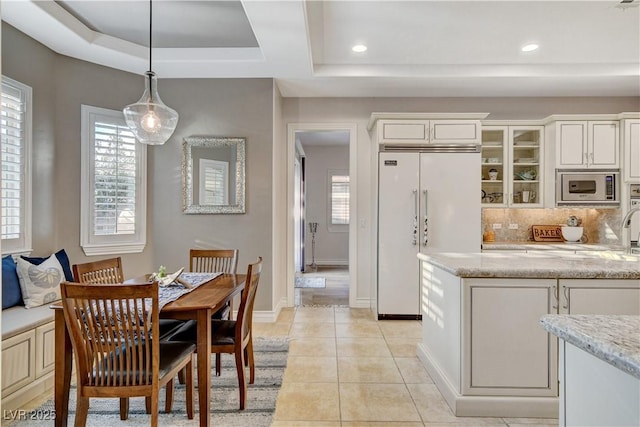 kitchen featuring light tile patterned flooring, decorative backsplash, glass insert cabinets, built in appliances, and a raised ceiling