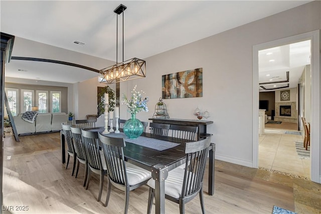 dining area featuring visible vents, a fireplace with raised hearth, light wood-style flooring, recessed lighting, and baseboards