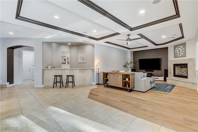 living area featuring light tile patterned floors, a fireplace, arched walkways, coffered ceiling, and a ceiling fan