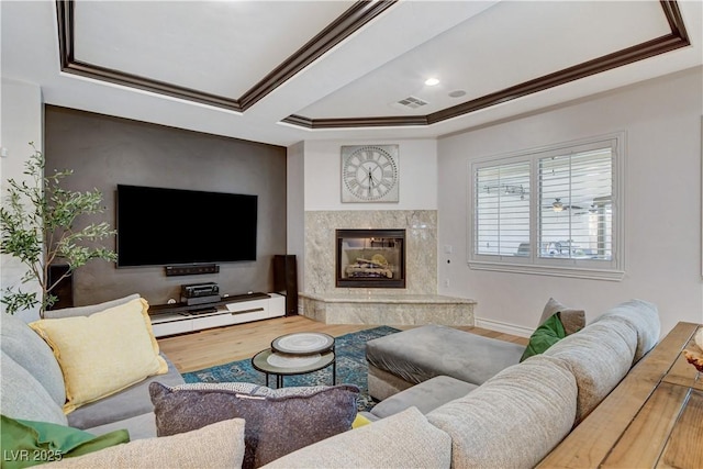 living area featuring a high end fireplace, visible vents, a tray ceiling, and wood finished floors