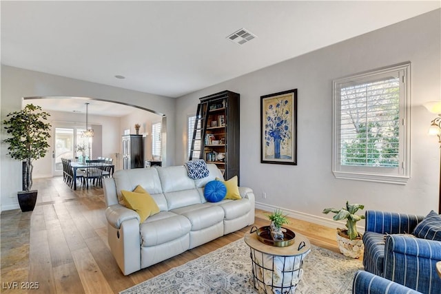 living room with arched walkways, visible vents, baseboards, and wood finished floors