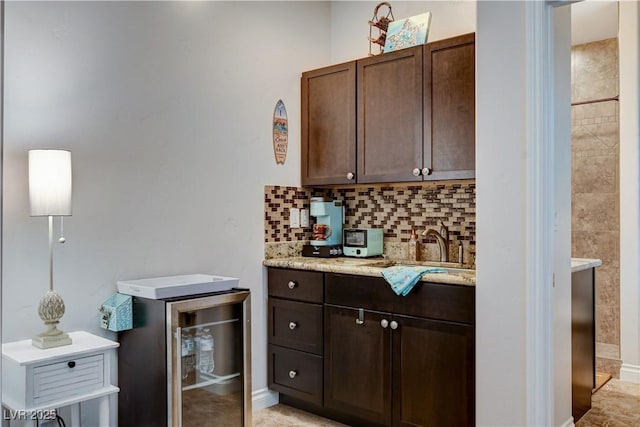 kitchen featuring tasteful backsplash, dark brown cabinets, light stone counters, and a sink