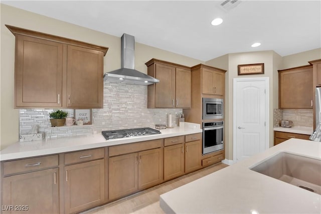 kitchen featuring visible vents, a sink, stainless steel appliances, light countertops, and wall chimney exhaust hood