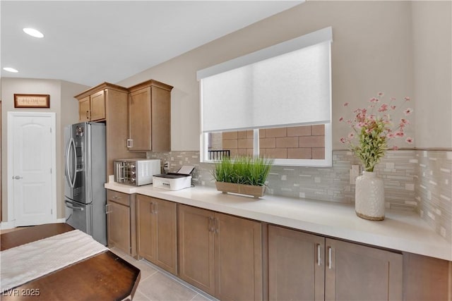 kitchen featuring tasteful backsplash, brown cabinetry, a toaster, stainless steel fridge with ice dispenser, and light countertops