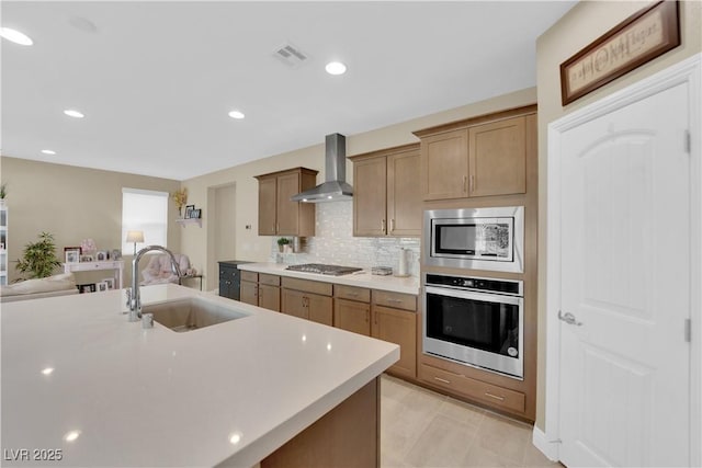 kitchen featuring visible vents, a sink, stainless steel appliances, light countertops, and wall chimney exhaust hood