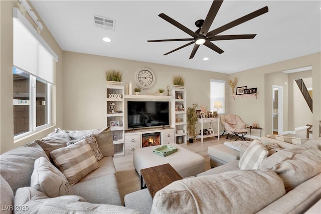 living area with a ceiling fan, visible vents, light wood-style flooring, recessed lighting, and a glass covered fireplace