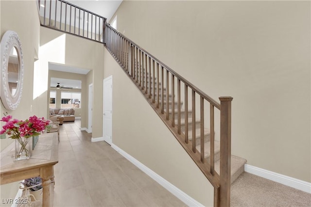 stairs with baseboards, a towering ceiling, and ceiling fan