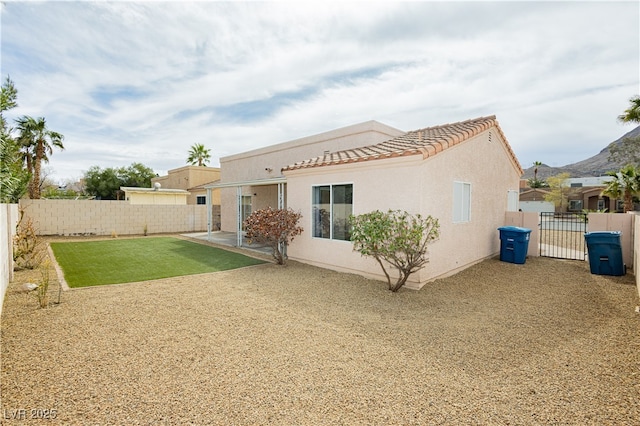 back of house featuring a gate, a fenced backyard, stucco siding, a tile roof, and a patio area