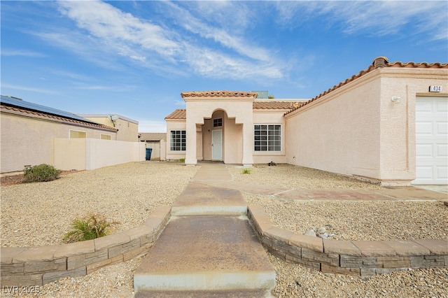 mediterranean / spanish-style home featuring stucco siding, fence, an attached garage, and a tile roof